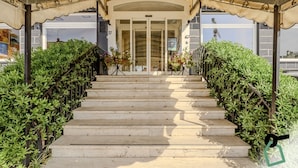 A set of stone steps leading to a building entrance under a covered area with a metal railing.