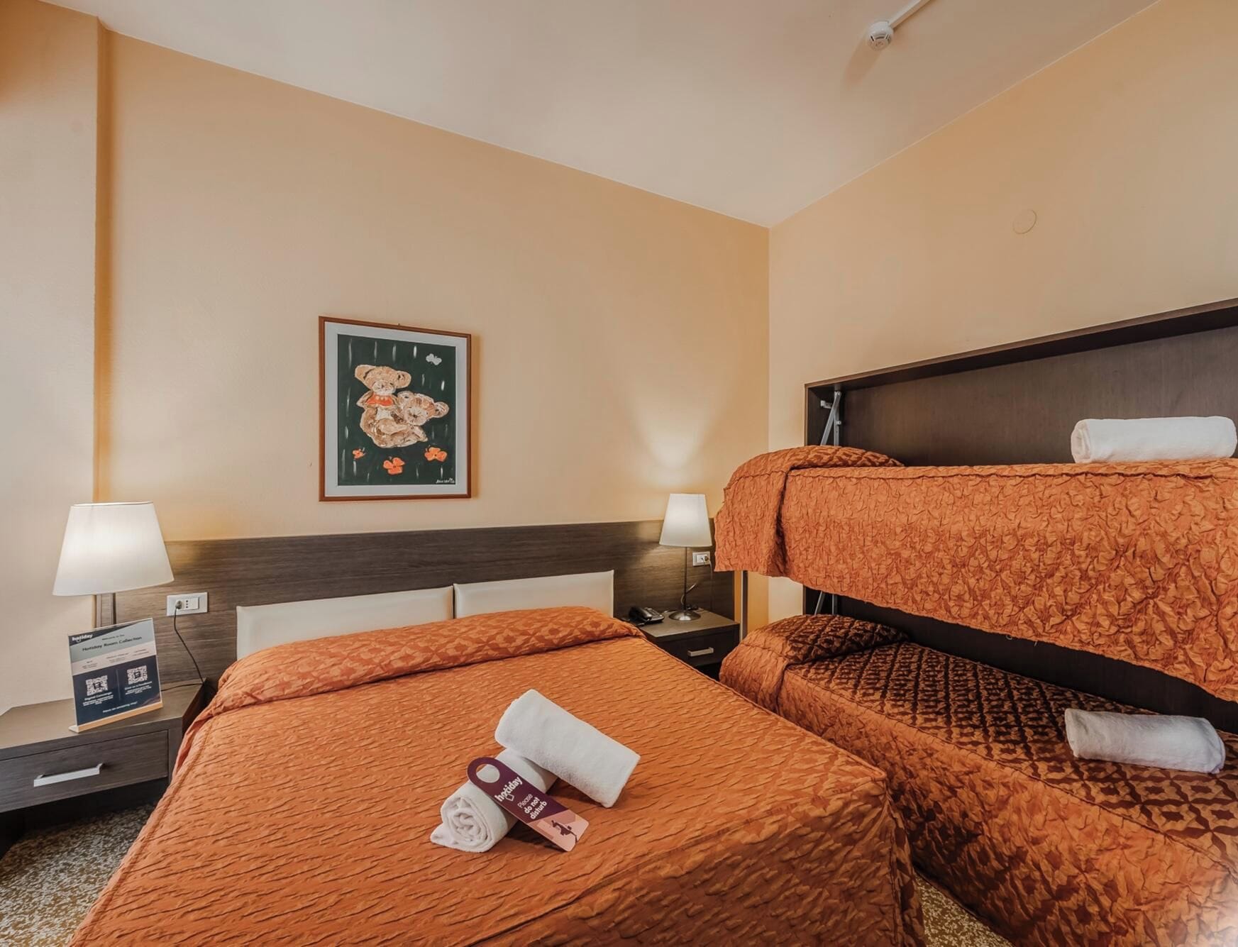 A hotel room with two beds, a nightstand, a lamp, a framed picture on the wall, and a sign with QR code.