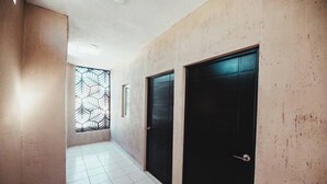 Ein Flur mit gefliestem Boden, zwei schwarzen Türen, einem Fenster mit Blattmuster und einem kleinen Fenster.