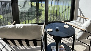 Een balkon met twee stoelen, een klein rond tafeltje en uitzicht op een meer en huizen.