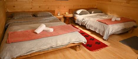 Un dormitorio de cabaña rústica con tres camas, pisos de madera y un ventanal pequeño.