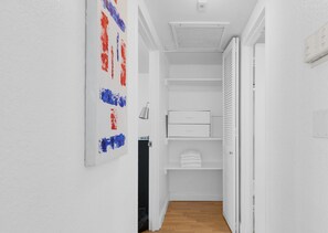 A narrow hallway with a white door on the right, a white wall with a red and blue abstract painting, and a white cabinet with a mirror. - Beautiful APT w/ Ocean View and Beach Access (Hollywood)