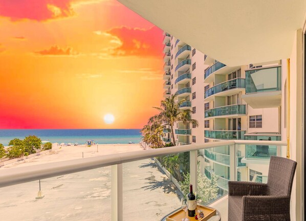 A balcony with a sunset view, a bottle of wine, and a glass on a tray. - Beautiful APT w/ Ocean View and Beach Access (Hollywood)
