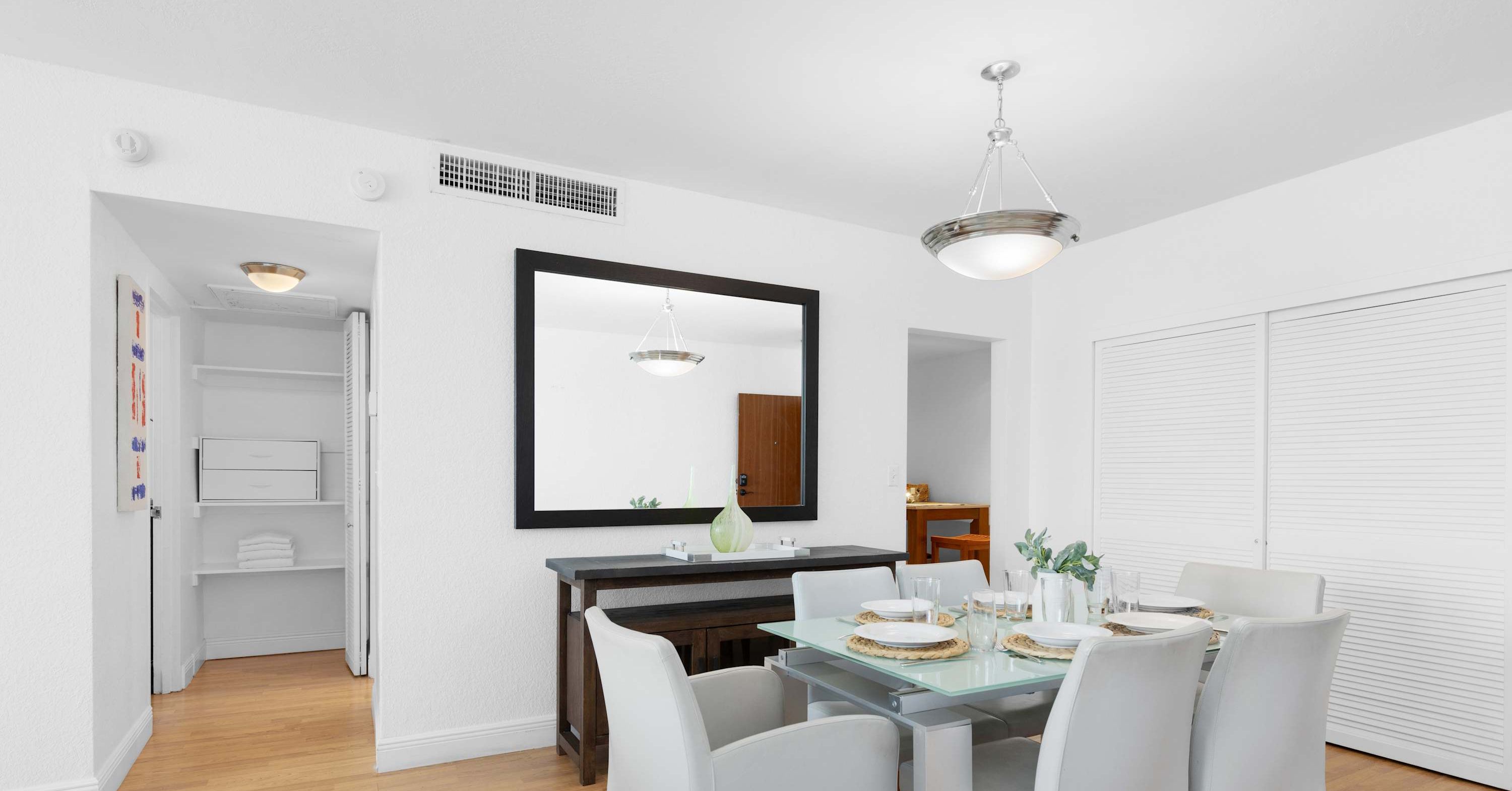 A dining area with a table set for four, a large mirror above the table, and a ceiling light fixture.