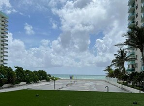A beachfront view with a grassy area, a lifeguard tower, and a building with balconies. - Beautiful APT w/ Ocean View and Beach Access (Hollywood)