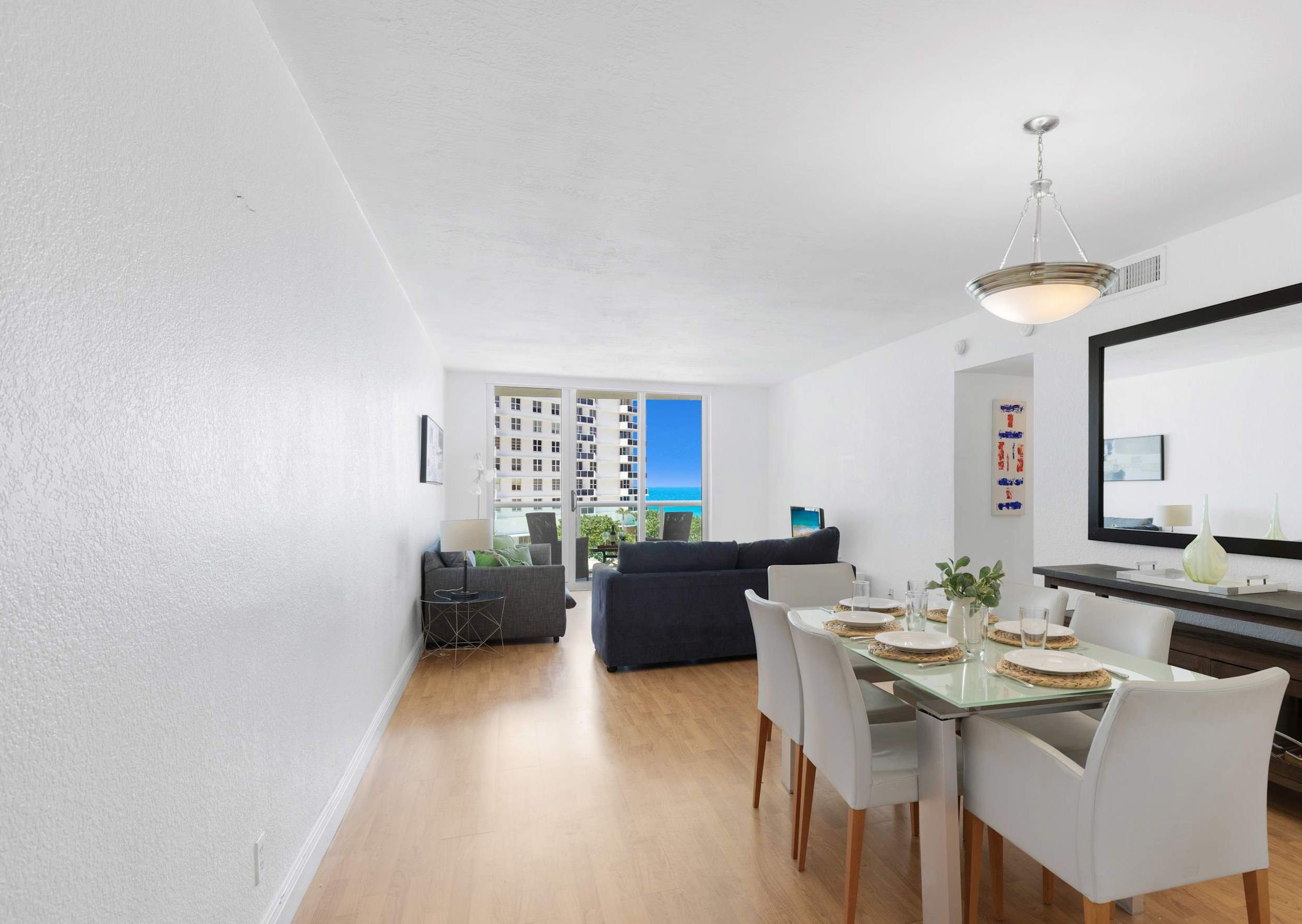 A modern living space with a dining area, a sofa, and a view of a building through a large window.