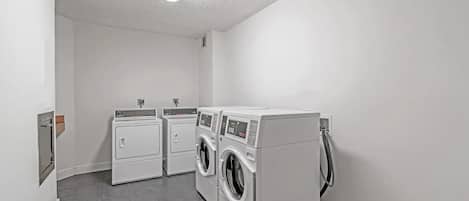 Une buanderie équipée de deux sèche-linge et de deux machines à laver, d’un luminaire fluorescent et d’une prise de courant au mur.