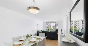 A modern dining area with a glass table, white plates, and a hanging light fixture. - Beautiful APT w/ Ocean View and Beach Access (Hollywood)