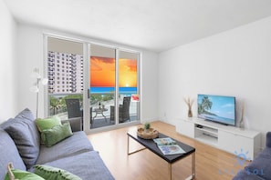 A modern living room with a sofa, a coffee table, and a TV on a white stand. - Beautiful APT w/ Ocean View and Beach Access (Hollywood)