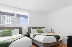 A hotel room with two beds, a window with a view of buildings, a bedside table with a lamp, and a tray with a bottle and glasses. - Beautiful APT w/ Ocean View and Beach Access (Hollywood)