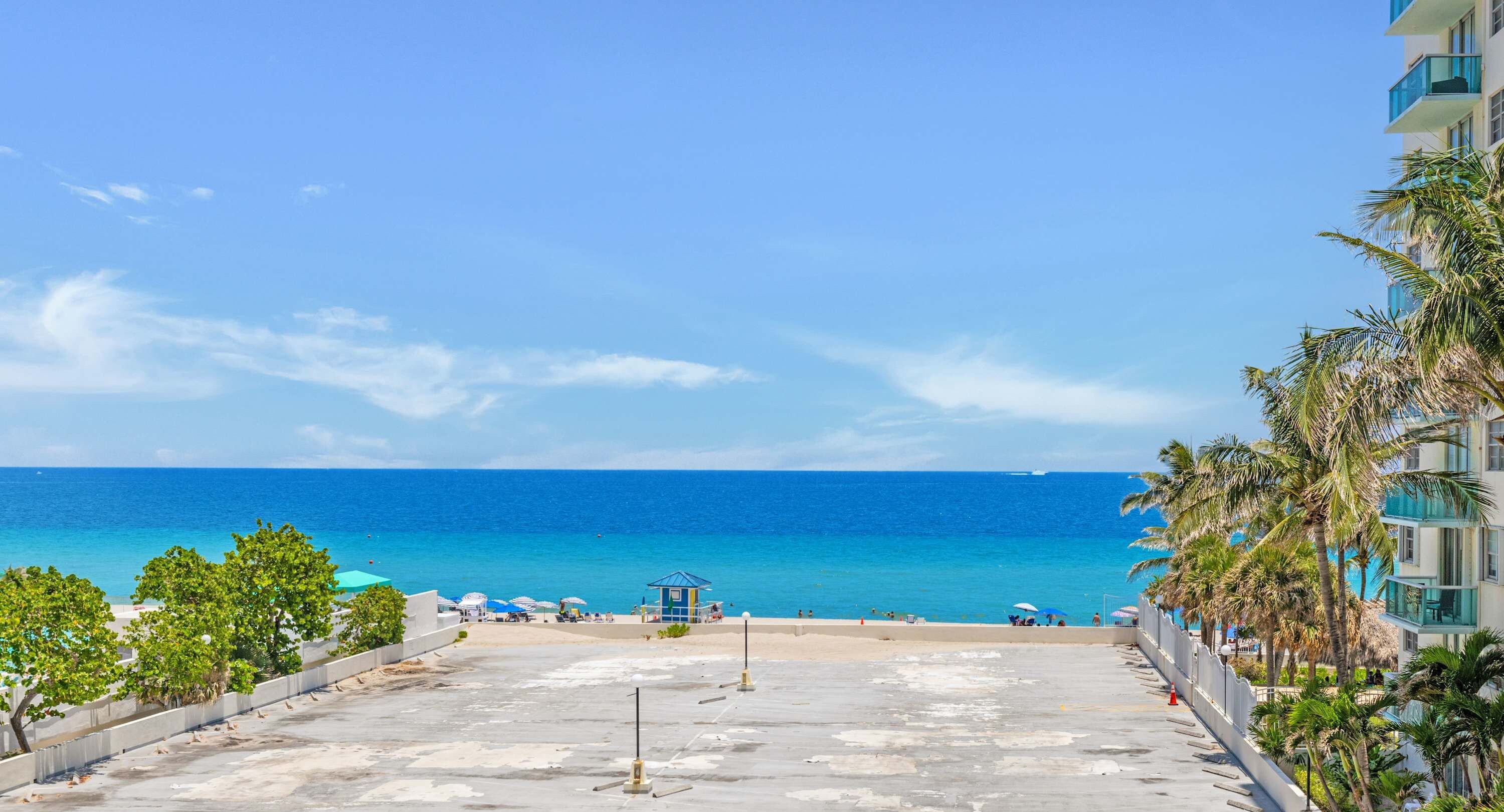 Vista frente al mar con cielo despejado, una playa arenosa y un edificio con balcones que dan al océano.