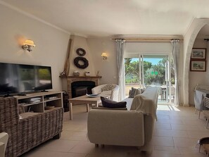 A living room with a TV, fireplace, wicker furniture, and a view of the outdoors. - Holiday home Bel Coll 8p airco pool and views (L'Escala)