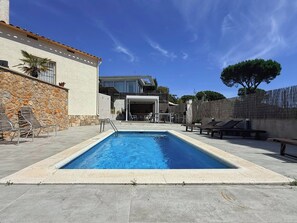 Une piscine avec des chaises longues, un mur en pierre et un bâtiment doté d’un balcon.