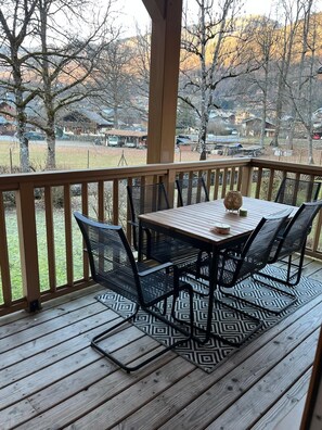 A covered outdoor deck with a table and chairs, a patterned rug, and a view of a residential area.