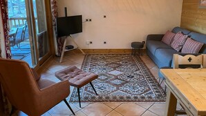 A living room with a TV on a stand, a sofa, a patterned rug, and a wooden table.