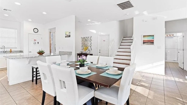 Una cocina moderna con armarios blancos, una isla central y un comedor con sillas blancas y una mesa de madera oscura.