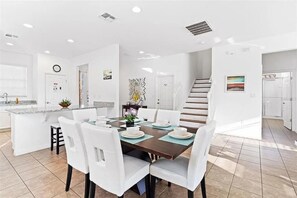 A modern kitchen with white cabinetry, a central island, and a dining area with white chairs and a dark wooden table. - Grand EXEC Golf 4BR Pool Home Near Disney (Davenport)