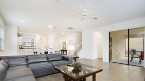 Una sala de estar moderna con un sofá seccional, una mesa de centro de vidrio y una cocina al fondo.