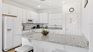 Una cocina moderna con gabinetes blancos, una encimera de granito y una pequeña isla con una planta.