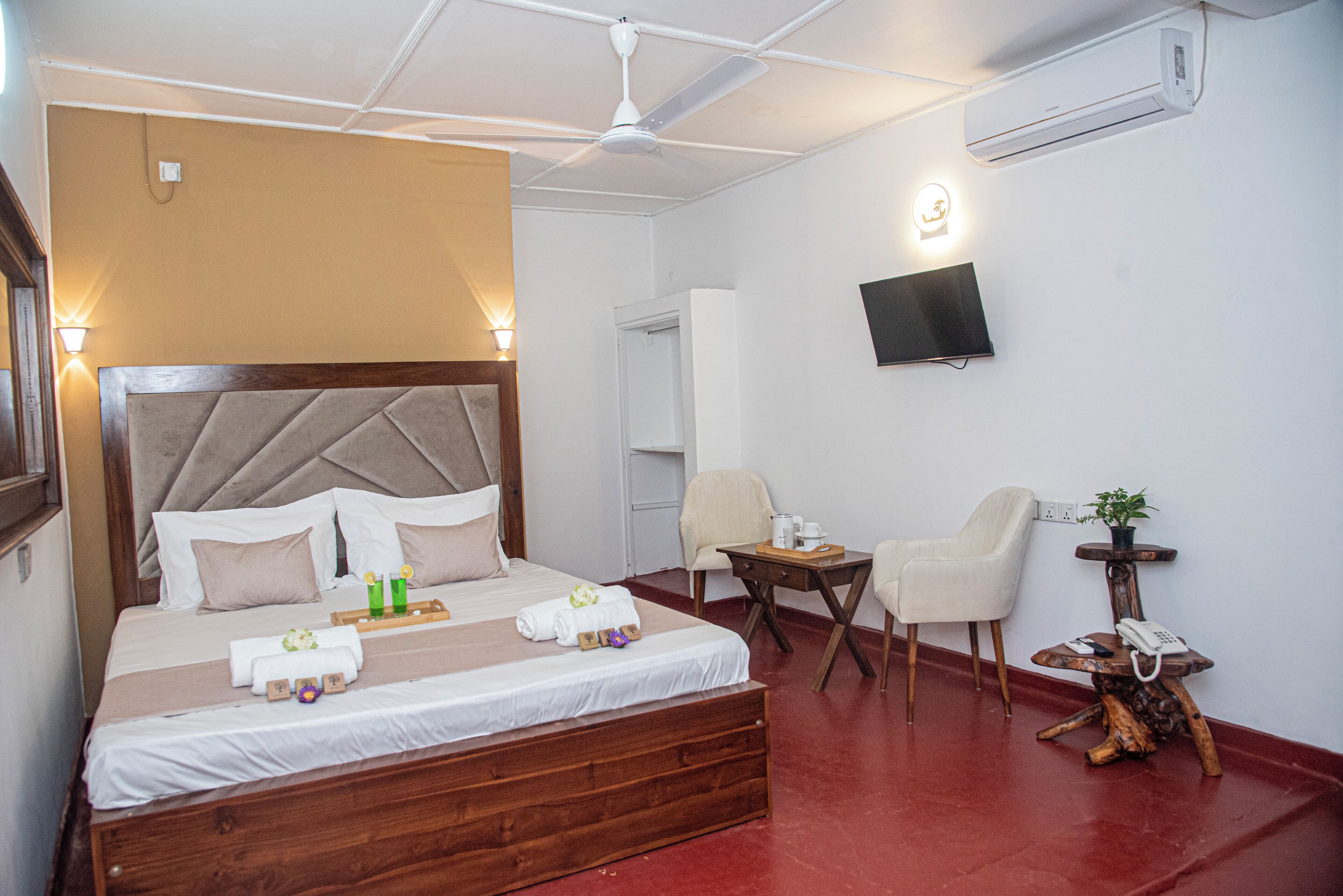 Una habitación de hotel con una cama, mesitas de noche, una silla, una pequeña mesa con una planta y un televisor montado en la pared.