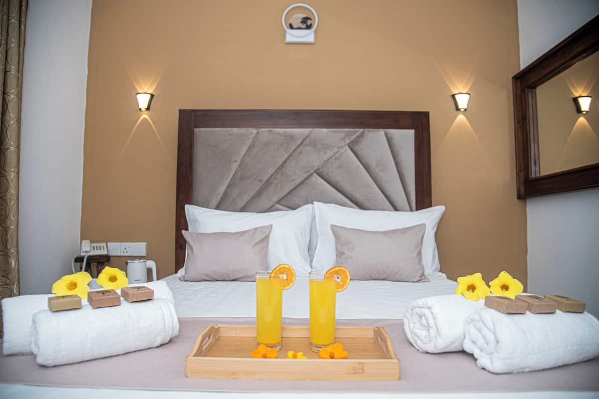 Una camera d'albergo con un letto, due comodini, un tavolino e un vassoio con due bicchieri di succo d'arancia e fiori.
