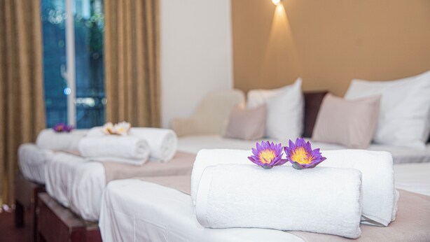 Ein Hotelzimmer mit zwei Betten, jeweils ausgestattet mit einem gerollten weißen Handtuch und einer violetten Lotusblume.