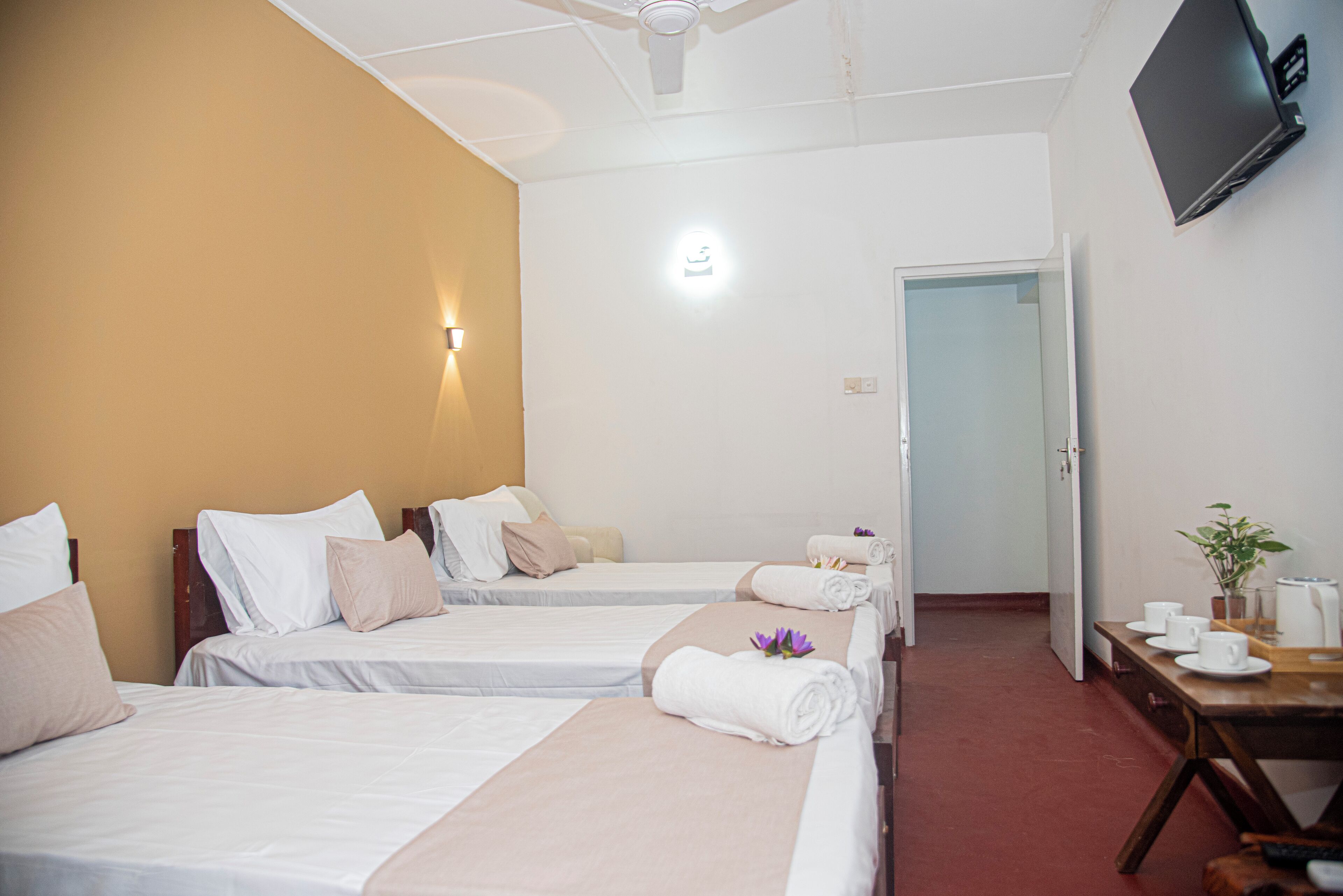 Habitación de hotel con dos camas, un escritorio con silla, un televisor y una puerta que da a otra habitación.
