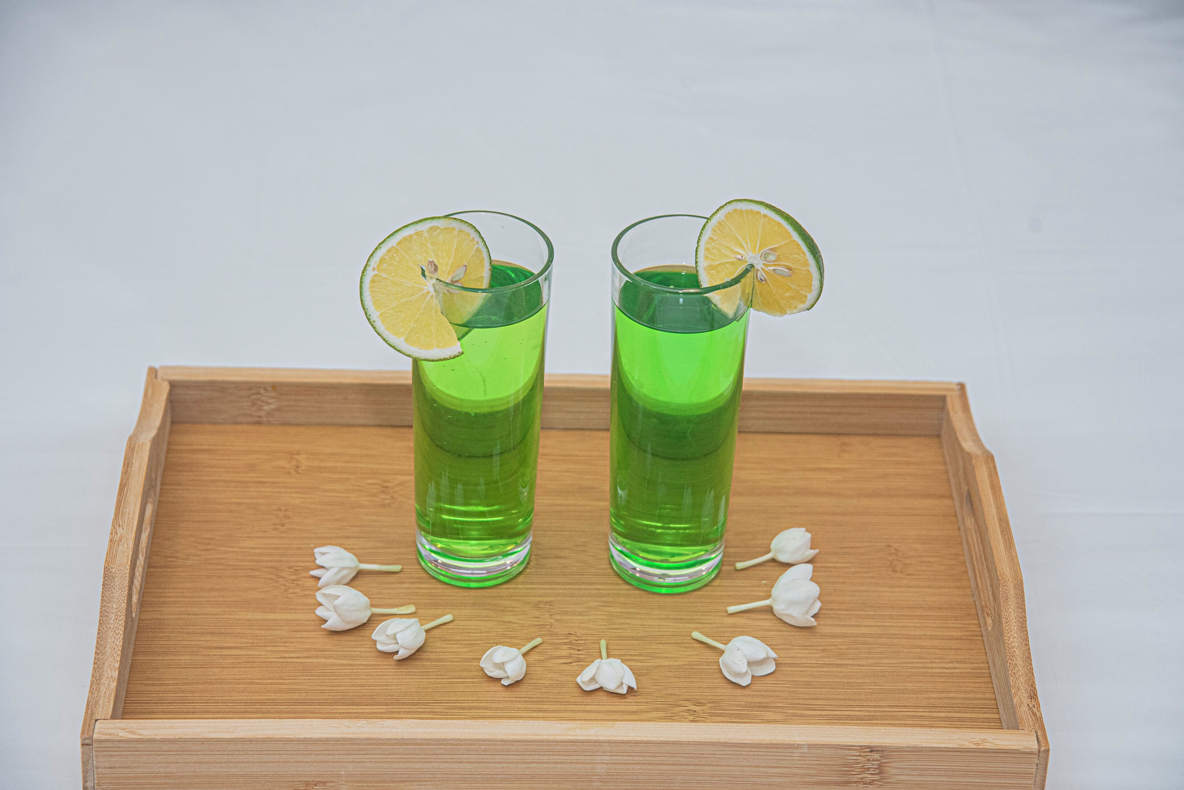 Two glasses of green liquid on a wooden tray with white flowers.