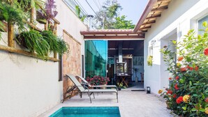 A poolside area with a tiled floor, a pool, lounge chairs, and a covered patio. - Bz35 Casa com piscina aquecida em Geribá (Buzios)