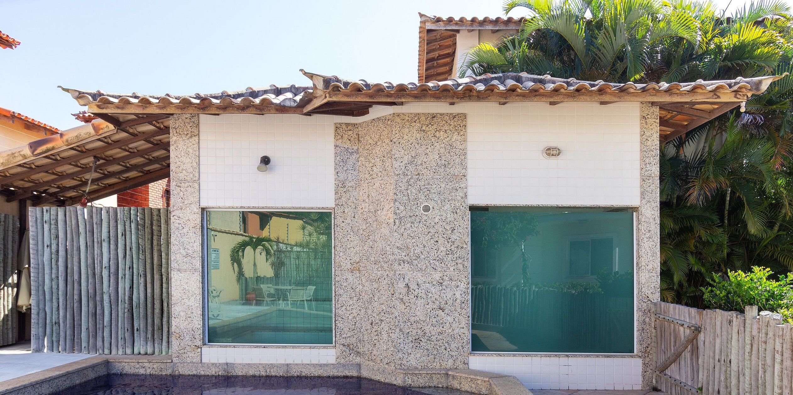 A building with a tiled roof, large windows, and a stone wall.