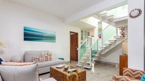 A living room with a sofa, a coffee table, and a staircase leading to an upper floor. - Bz35 Casa com piscina aquecida em Geribá (Buzios)
