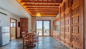 A spacious kitchen with a dining area, wooden cabinets, and a stone floor. - Arte Pefki Beachfront Suites (Rhodes)