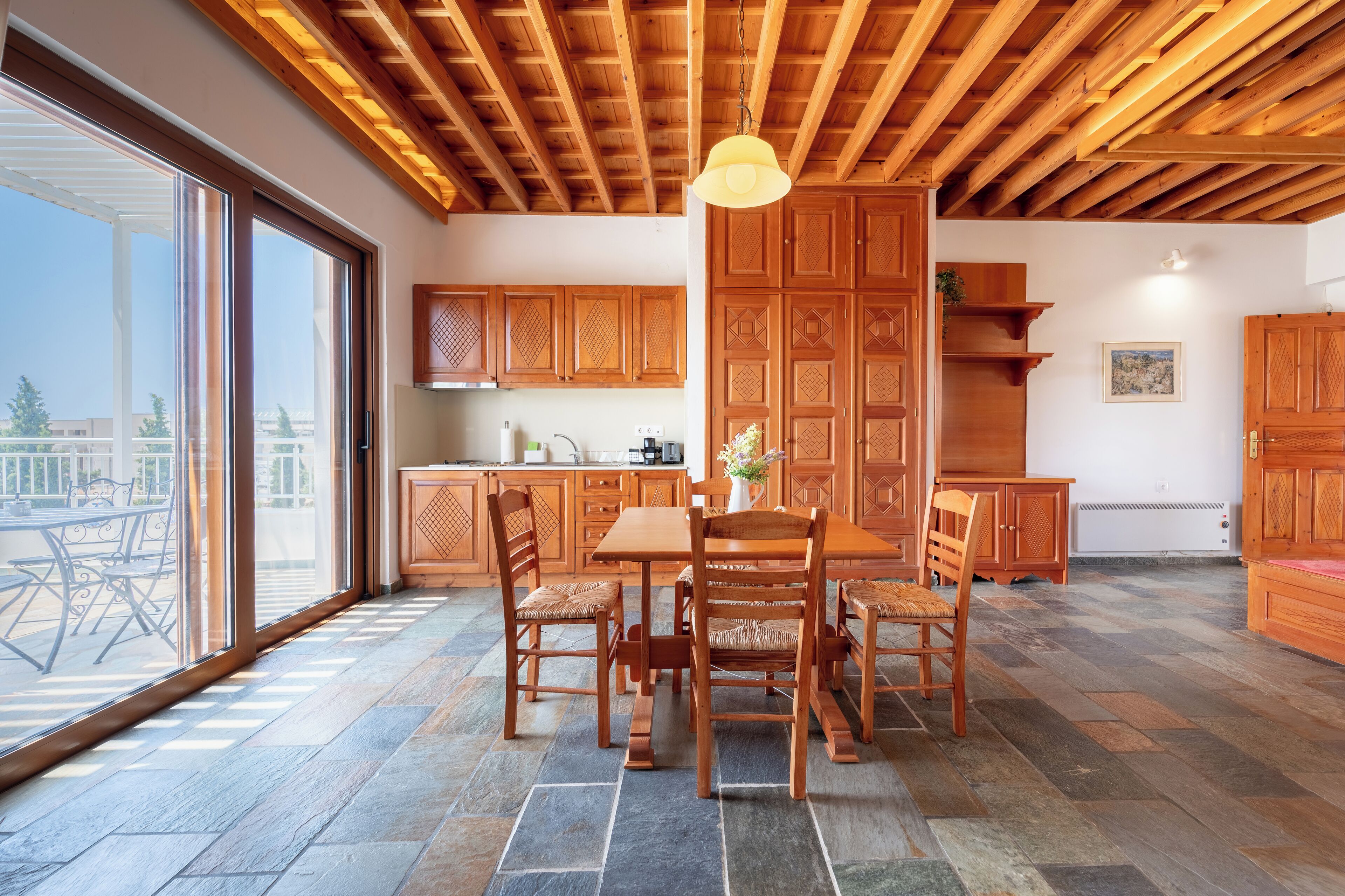 A spacious kitchen with wooden cabinets, a dining table with chairs, and a large window with a view of the outdoors.