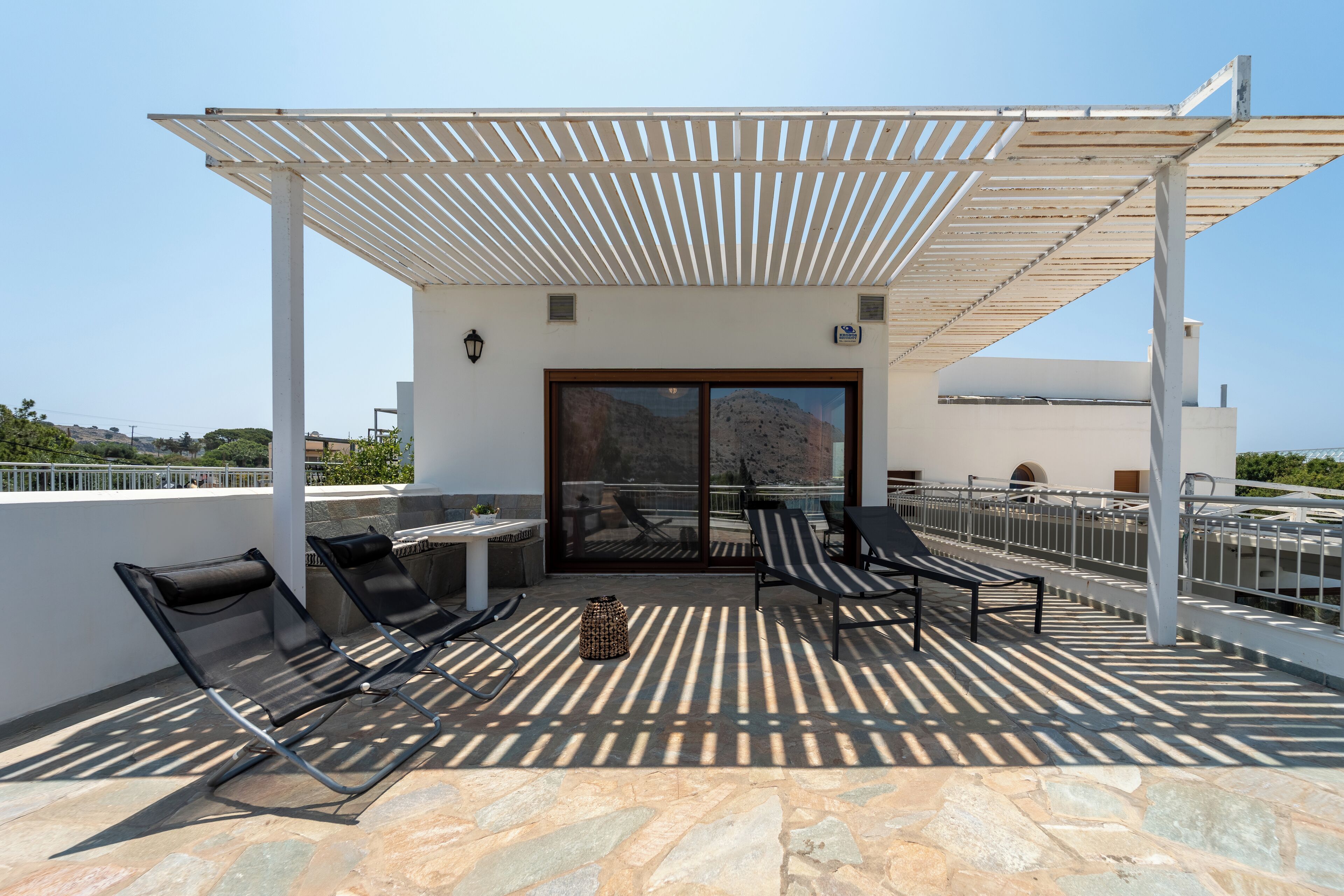 Une terrasse sur le toit dotée d’une pergola, de chaises longues et d’un sol en pierre.