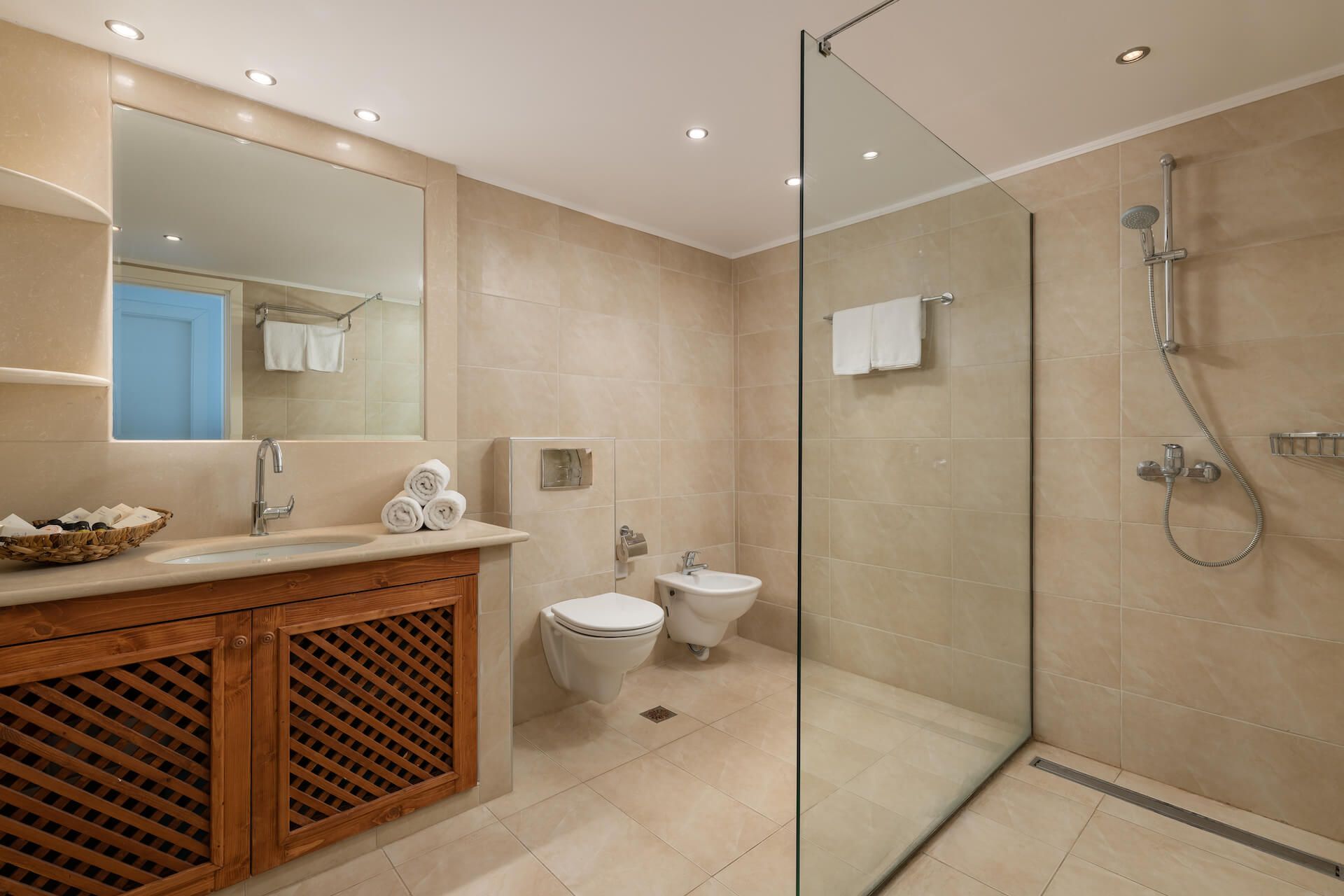 A modern bathroom with a glass-enclosed shower, a wooden vanity with a sink, and two toilets.