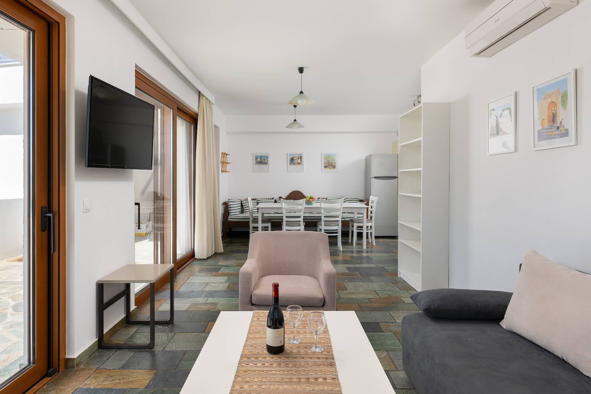 A modern living room with a sofa, a dining table with chairs, a TV mounted on the wall, and a refrigerator.
