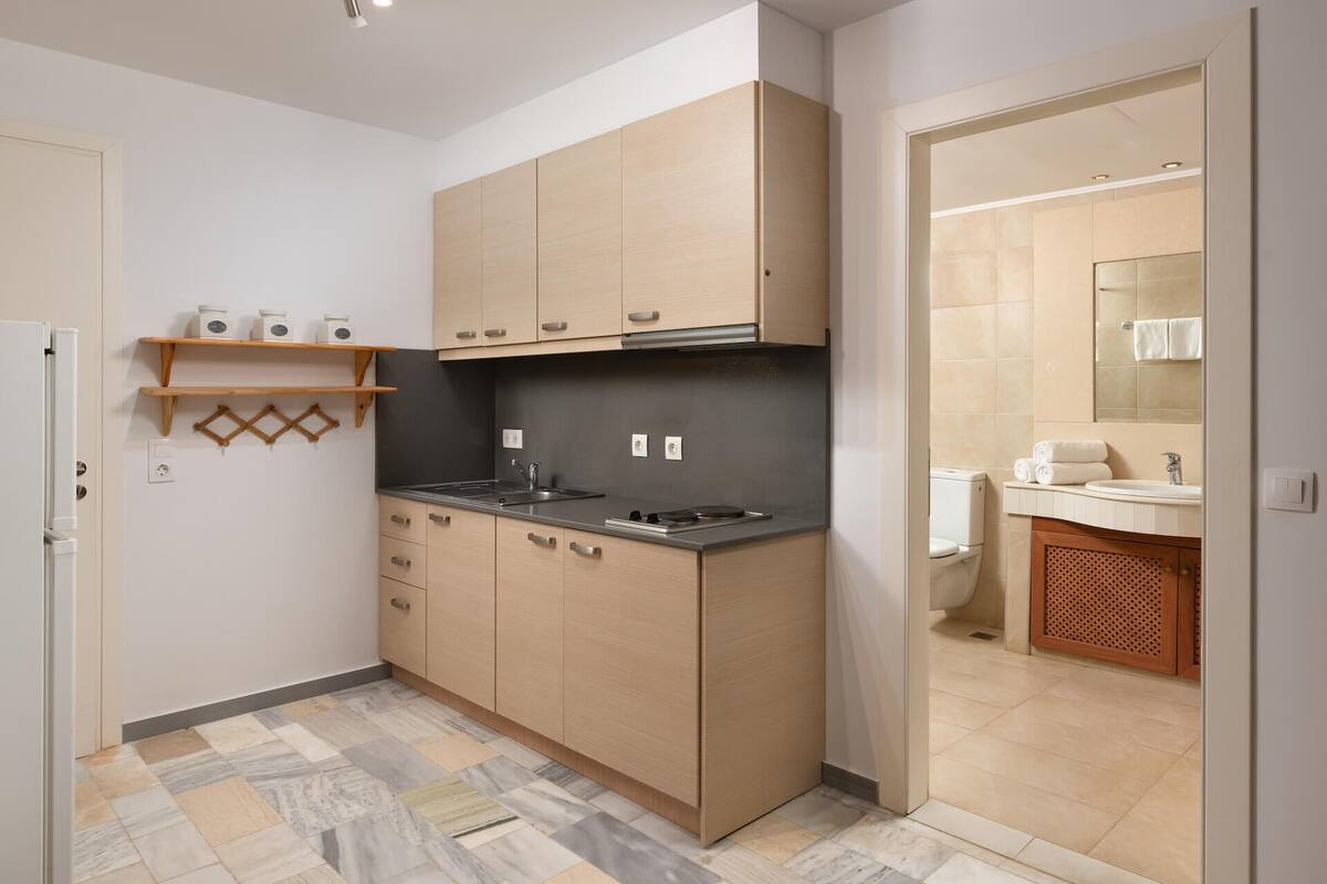 A compact kitchen with a stove, sink, and cabinets. There is a small shelf with jars and a hanging rack.