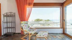A balcony with a chair and ottoman, a metal shelf, and a view of a bridge and greenery. - Arte Pefki Beachfront Suites (Rhodes)