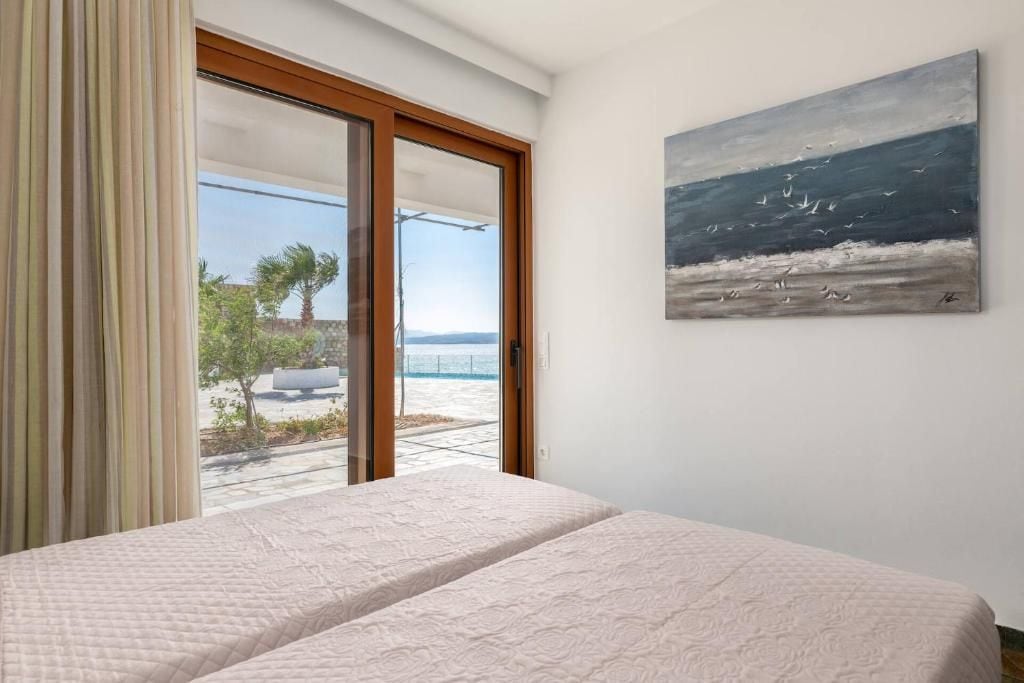 Un dormitorio con una cama grande, un cerramiento de vidrio corredero que da a un balcón y un cuadro de un paisaje marino.