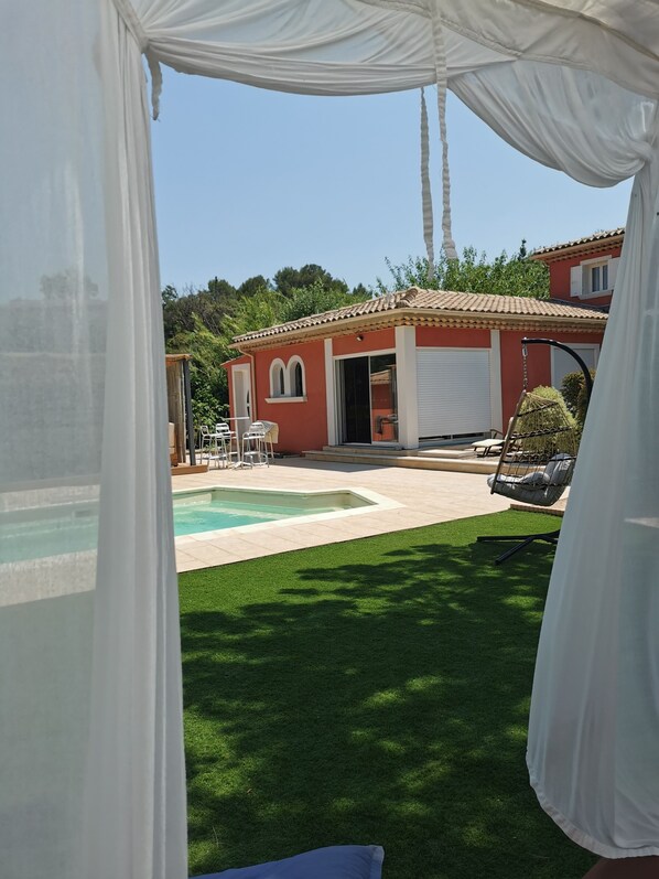 A pool area with a red building, outdoor furniture, and a swing chair.