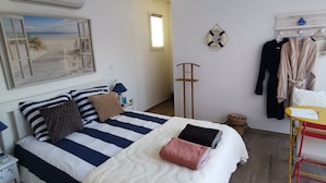 A bedroom with a bed, a small table, a chair, a wall-mounted shelf, and a window.