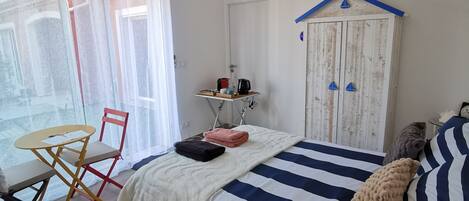 Un dormitorio con cama, mesita de noche, silla y una pequeña mesa con lámpara.