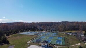 An aerial view of a tennis court complex with multiple courts, surrounded by trees and a clear sky. - Spacious little condo at SML- Mariner's Landing Resort (Huddleston)