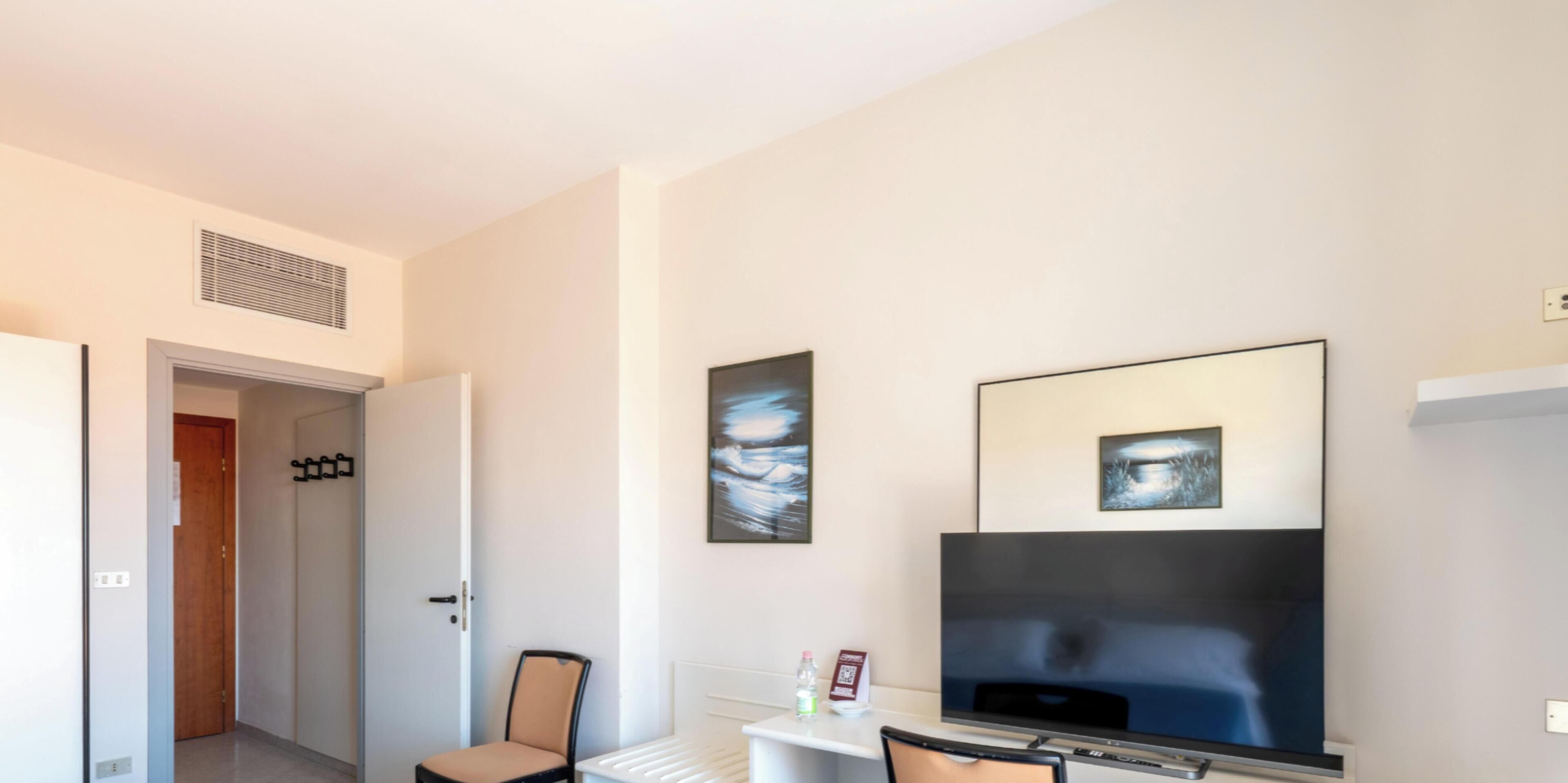 Habitación de hotel con cama, televisor, una silla y obras de arte en la pared.