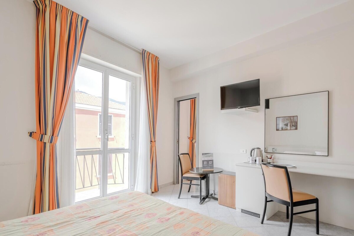 A hotel room with a bed, a desk, a chair, a TV, and a door.