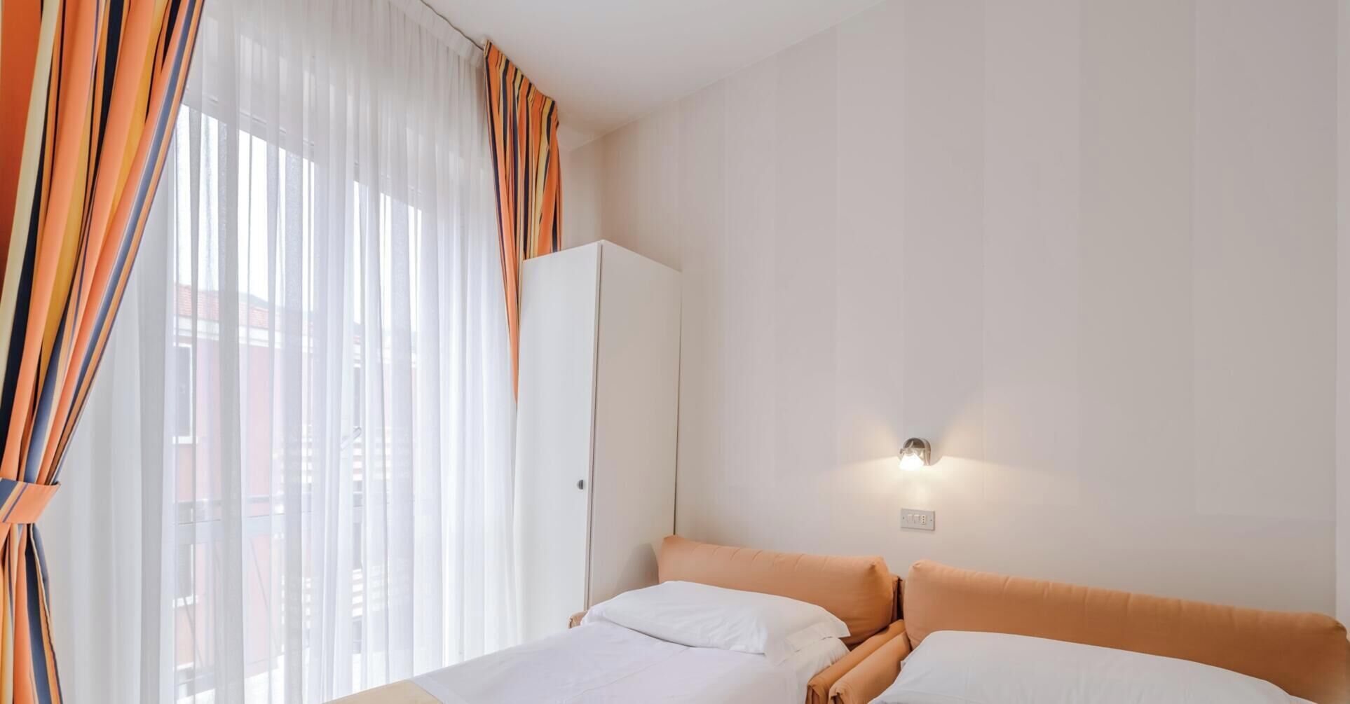 Una camera d'albergo con un letto, un armadio e una lampada fissata al muro.
