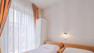 Una camera d'albergo con un letto, un armadio e una lampada fissata al muro.