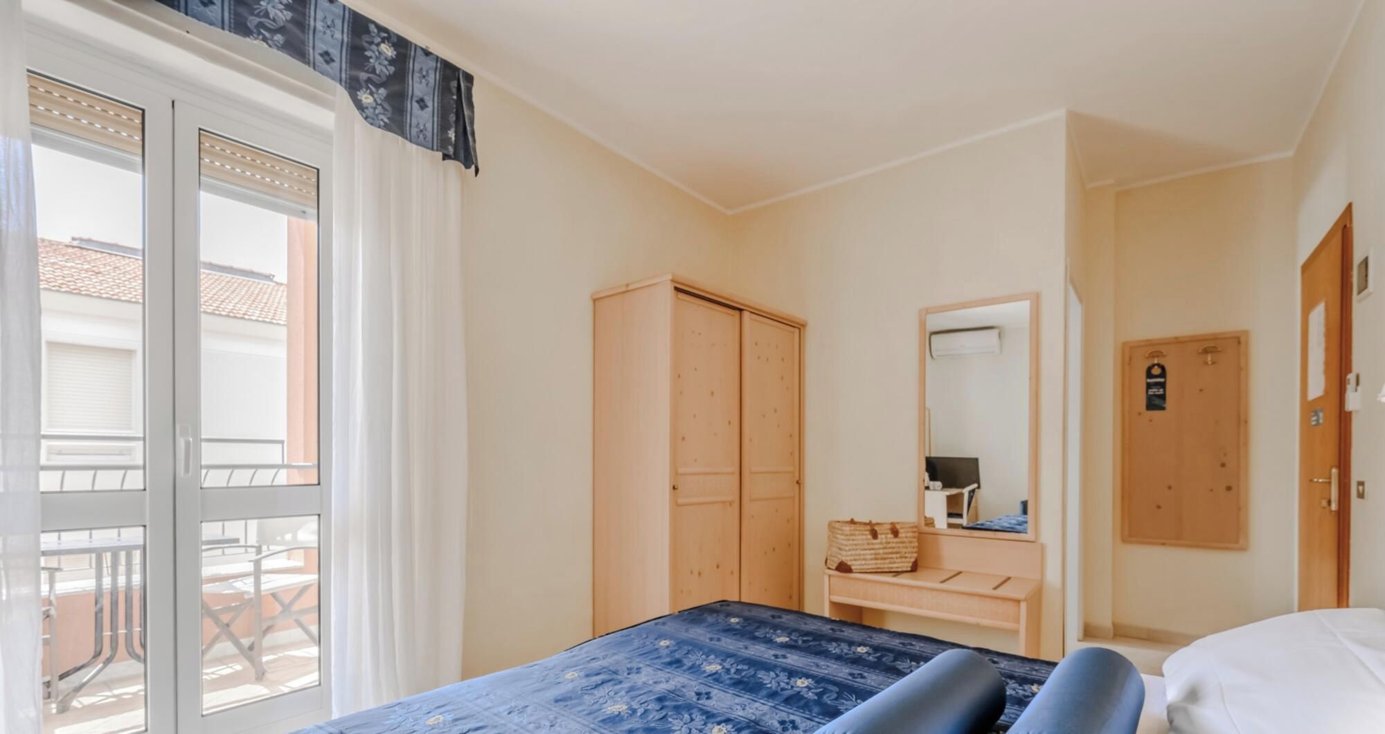 Ein Hotelzimmer mit Bett, Schrank, Schreibtisch mit Spiegel und Fenster mit Ausblick.