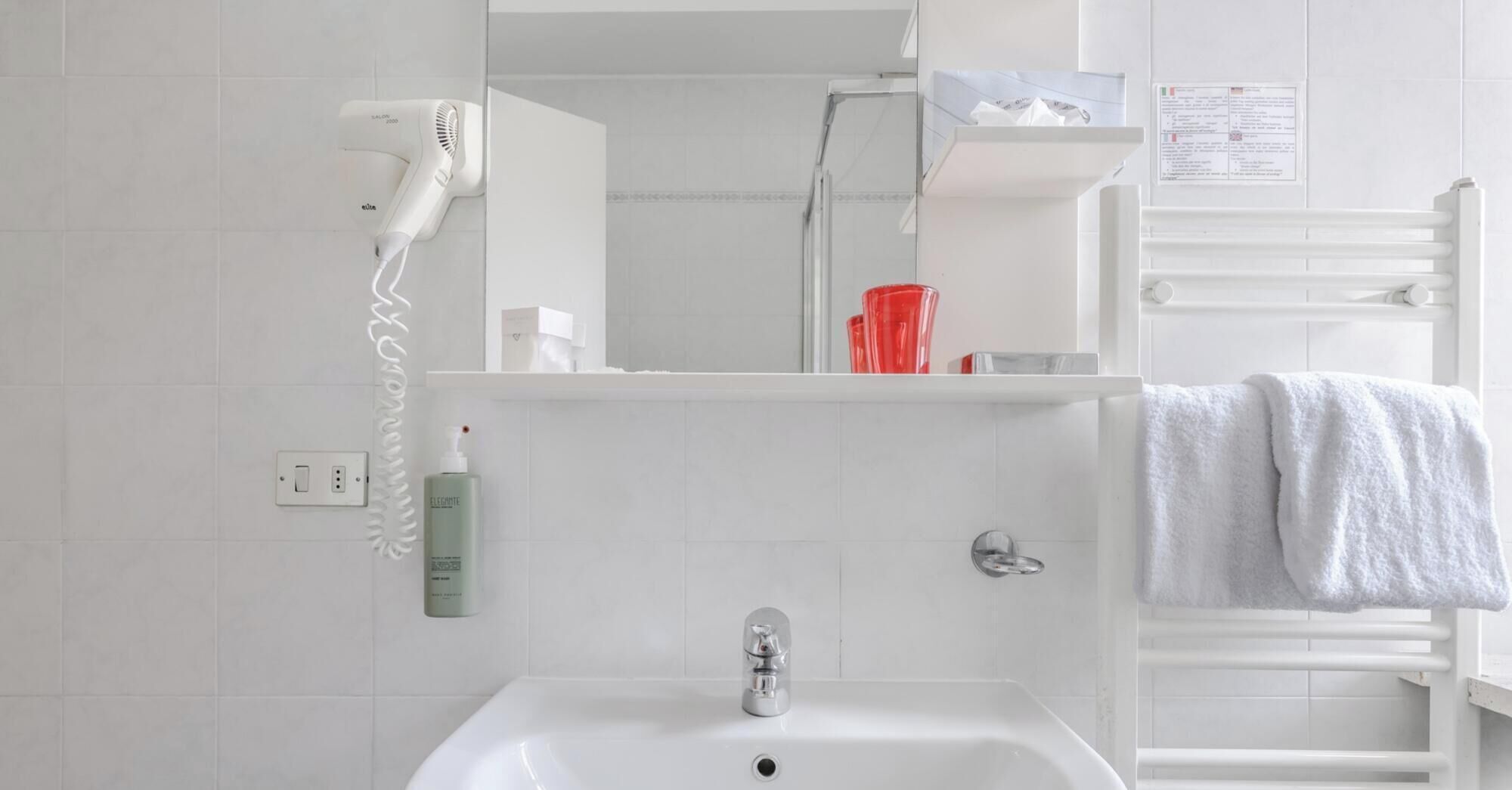 Ein Badezimmer mit einem weißen Waschbecken, einem an der Wand befestigten Föhn, einer roten Glasvase und einem Handtuchhalter mit einem Handtuch.