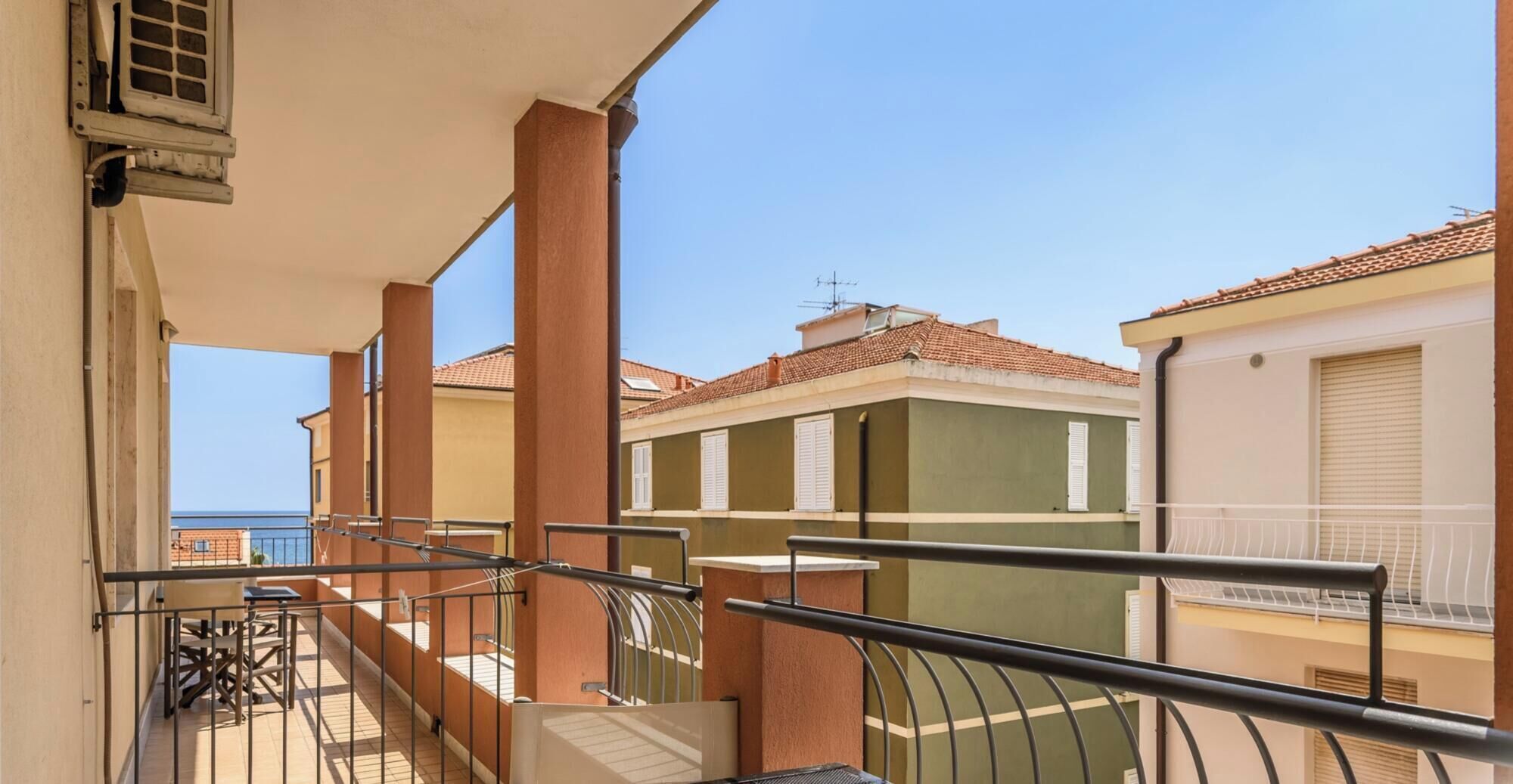 A balcony with a metal railing, a view of neighboring buildings, and a clear sky.